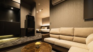 Quarto de hotel moderno com sofá, mesinha de centro com flores, televisão e minibar.
