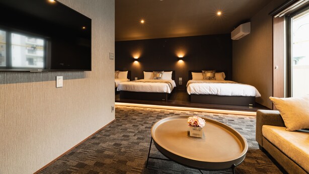 Quarto de hotel moderno com duas camas, um sofá, uma mesa de centro e uma televisão.
