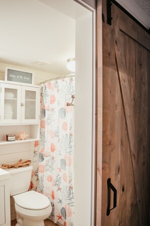 Een badkamer met een toilet, een kast en een douchegordijn met een zeemeerpatroon.
