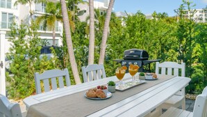 Ein weißer Tisch mit einem Grill, zwei Orangensaftgläsern, einem Tablett mit Croissants und einer kleinen Topfpflanze.