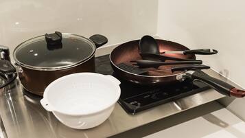 A kitchen with a stainless steel stove, a brown pot with a lid, a white colander, and a frying pan with black utensils.