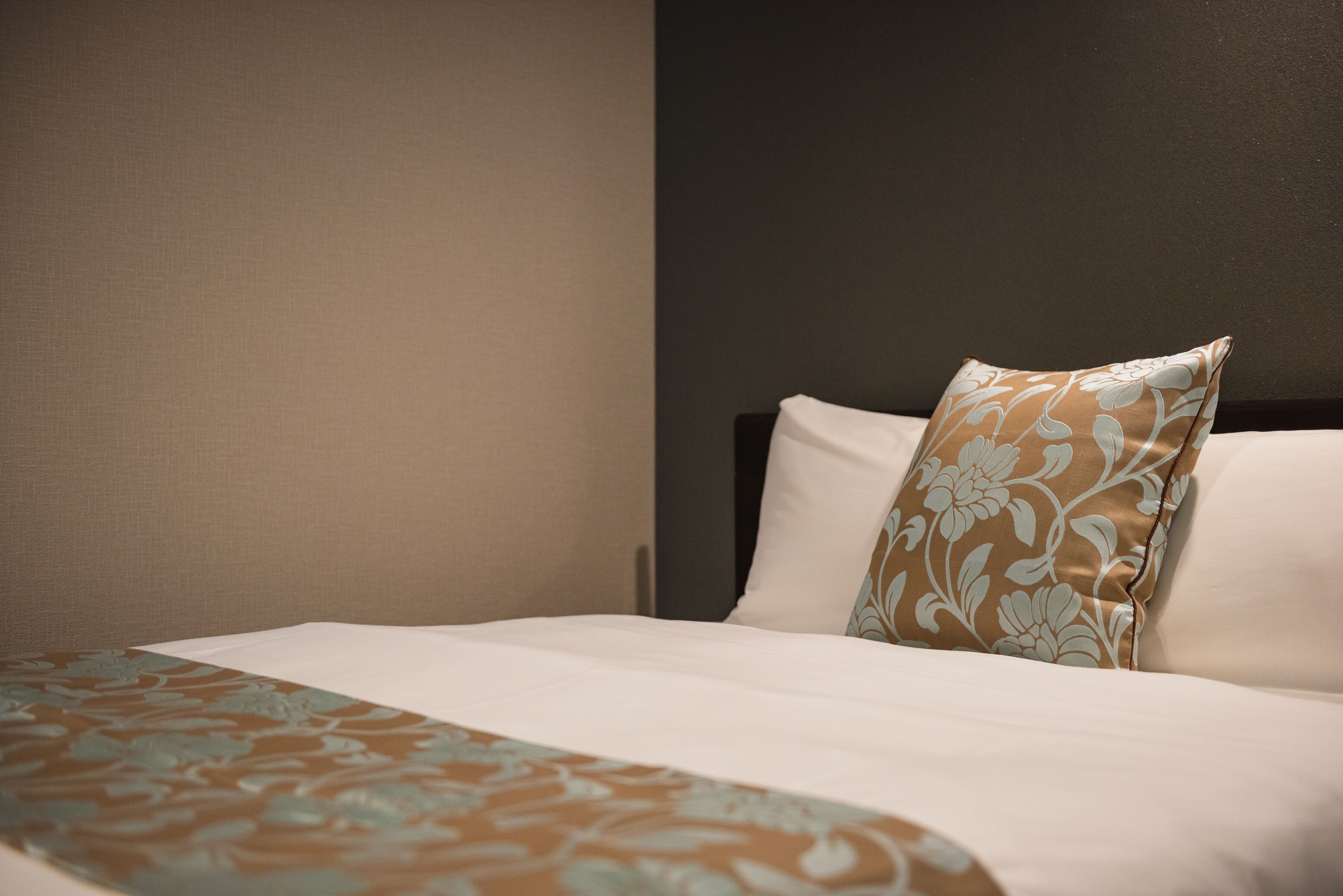 Un letto rifatto con cura, con una coperta a fantasia e un cuscino decorativo.