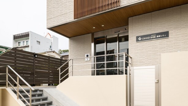 A hotel entrance with a staircase leading up to a door, a sign indicating the hotel name, and a modern building facade. - Grand Base Nagasaki City (Nagasaki)