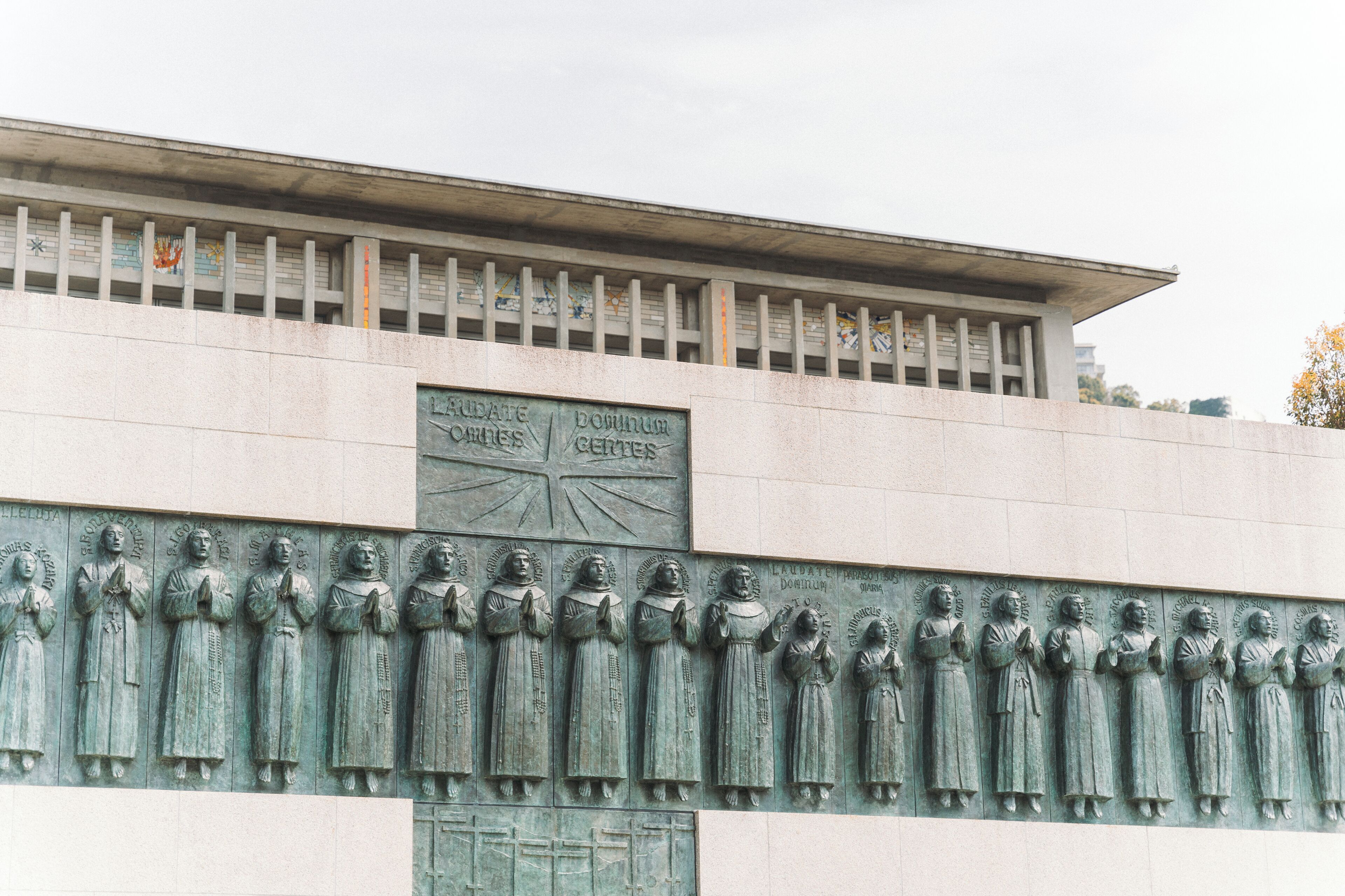 A building facade with a relief sculpture of multiple figures and a plaque with inscriptions.