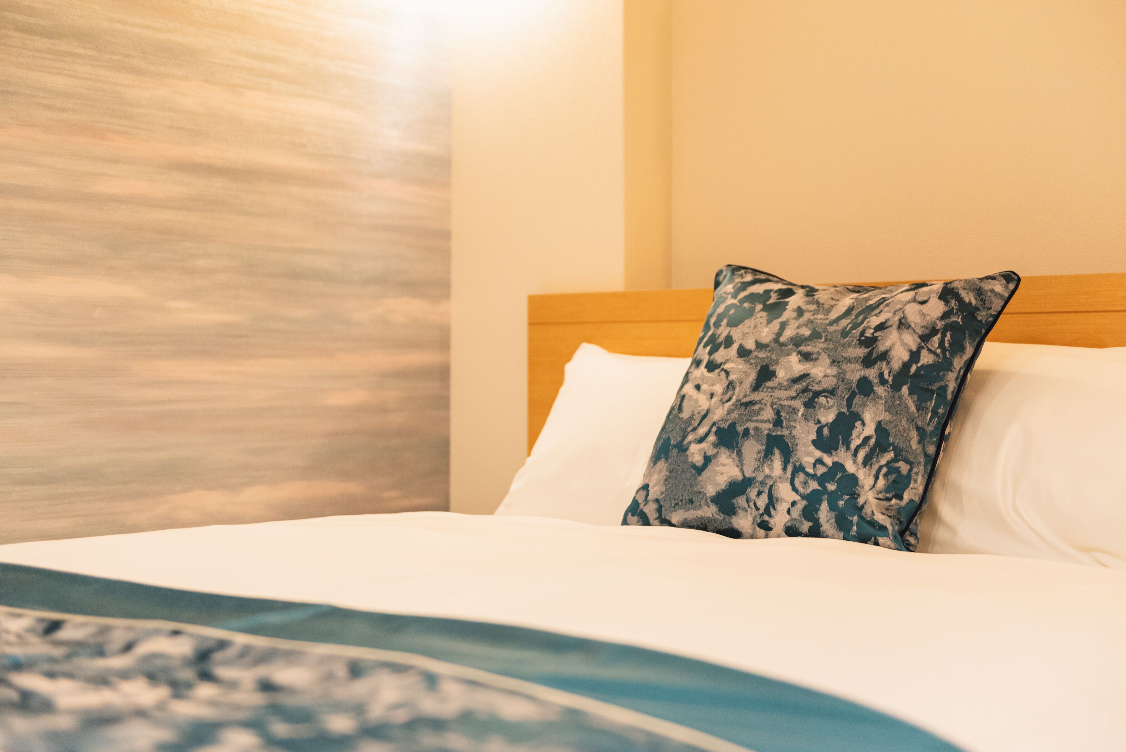 A neatly made bed with a patterned pillow and a blue and white blanket.