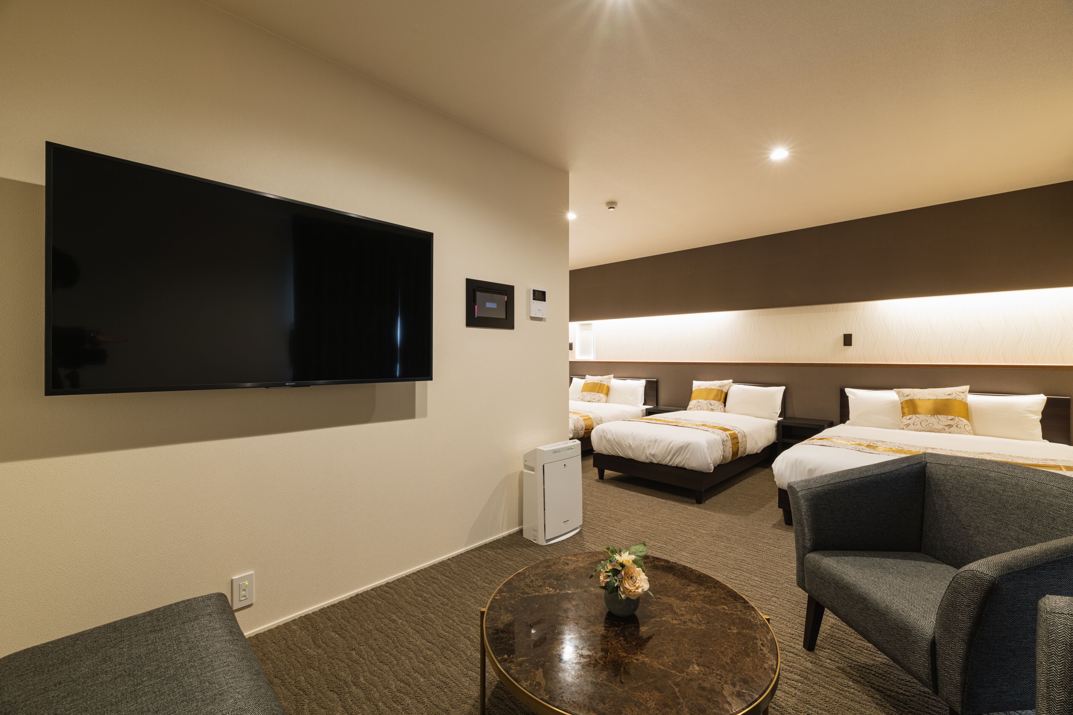 Habitación de hotel con televisión de pantalla plana, dos camas, una mesa de centro con un florero y una zona de estar con una silla.