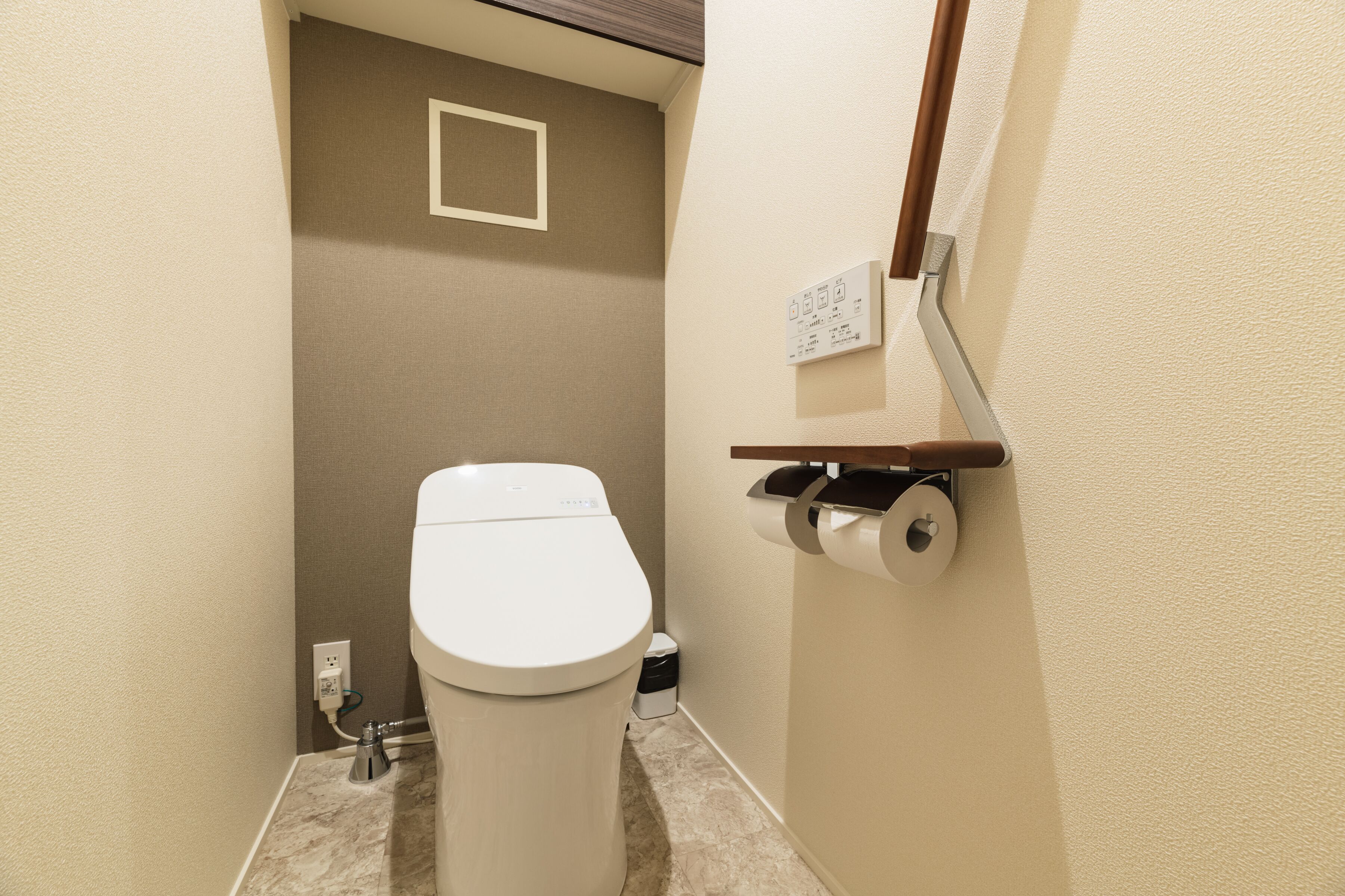 A small, compact bathroom with a toilet, a trash bin, and a toilet paper holder mounted on the wall.