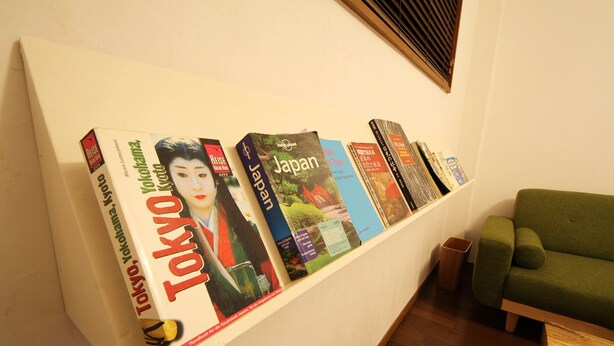 A bookshelf with travel books, a green sofa, and a wooden floor. - Sumica Apartments (Nikko)