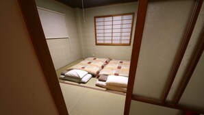 A traditional Japanese room with tatami flooring, a futon bed, shoji screens, and a sliding door. - Sumica Apartments (Nikko)