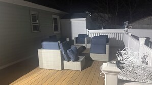 Una terraza con mobiliario de mimbre, incluyendo sillas y una mesa, y una barandilla blanca.
