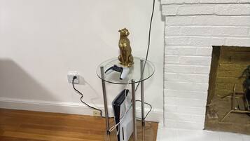 Un soggiorno con un tavolo in vetro su cui si trova una console per videogiochi e un controller, un camino in mattoni bianchi e un quadro appeso al muro.
