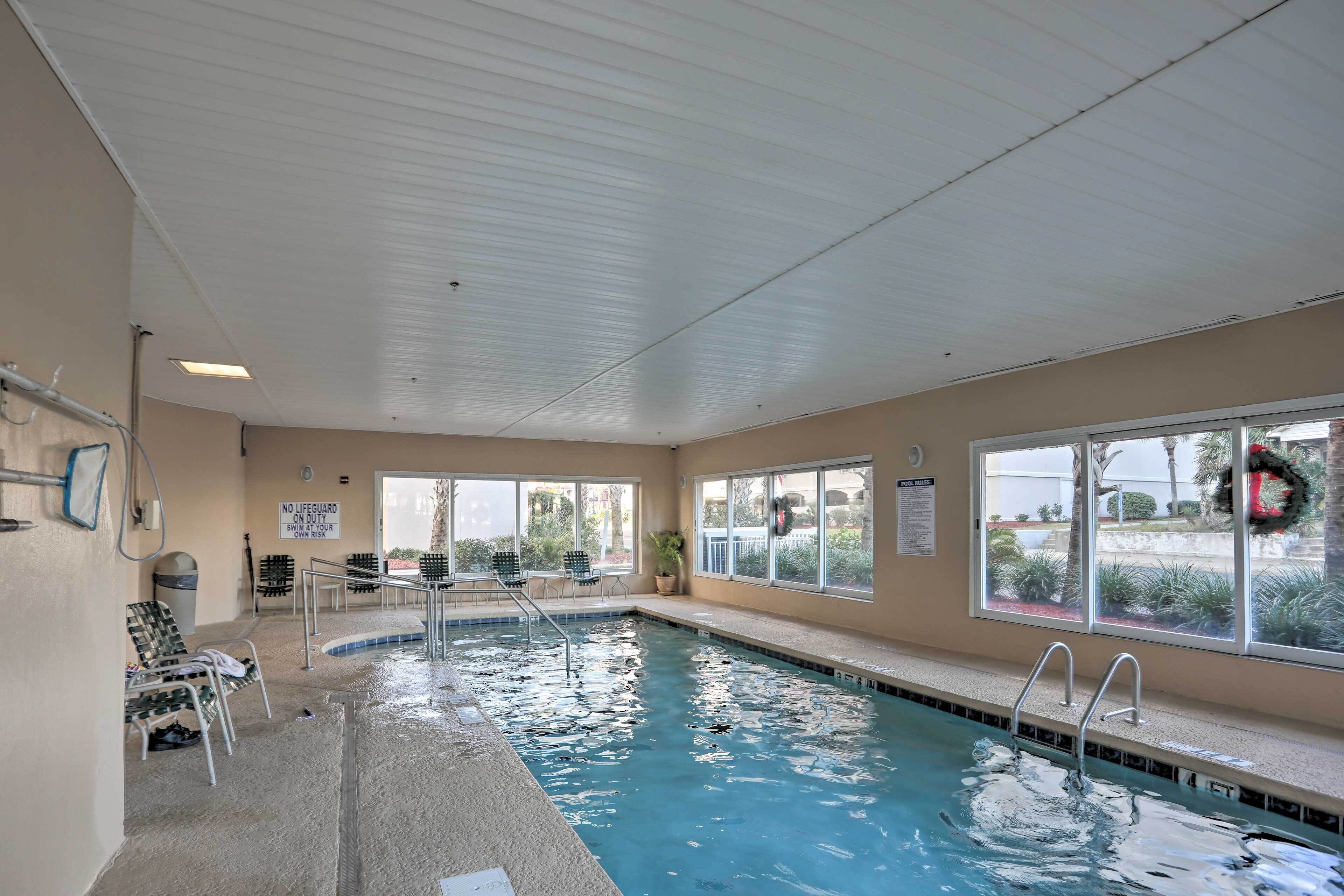 An indoor swimming pool with clear water, surrounded by windows and a no-lifeguard sign.