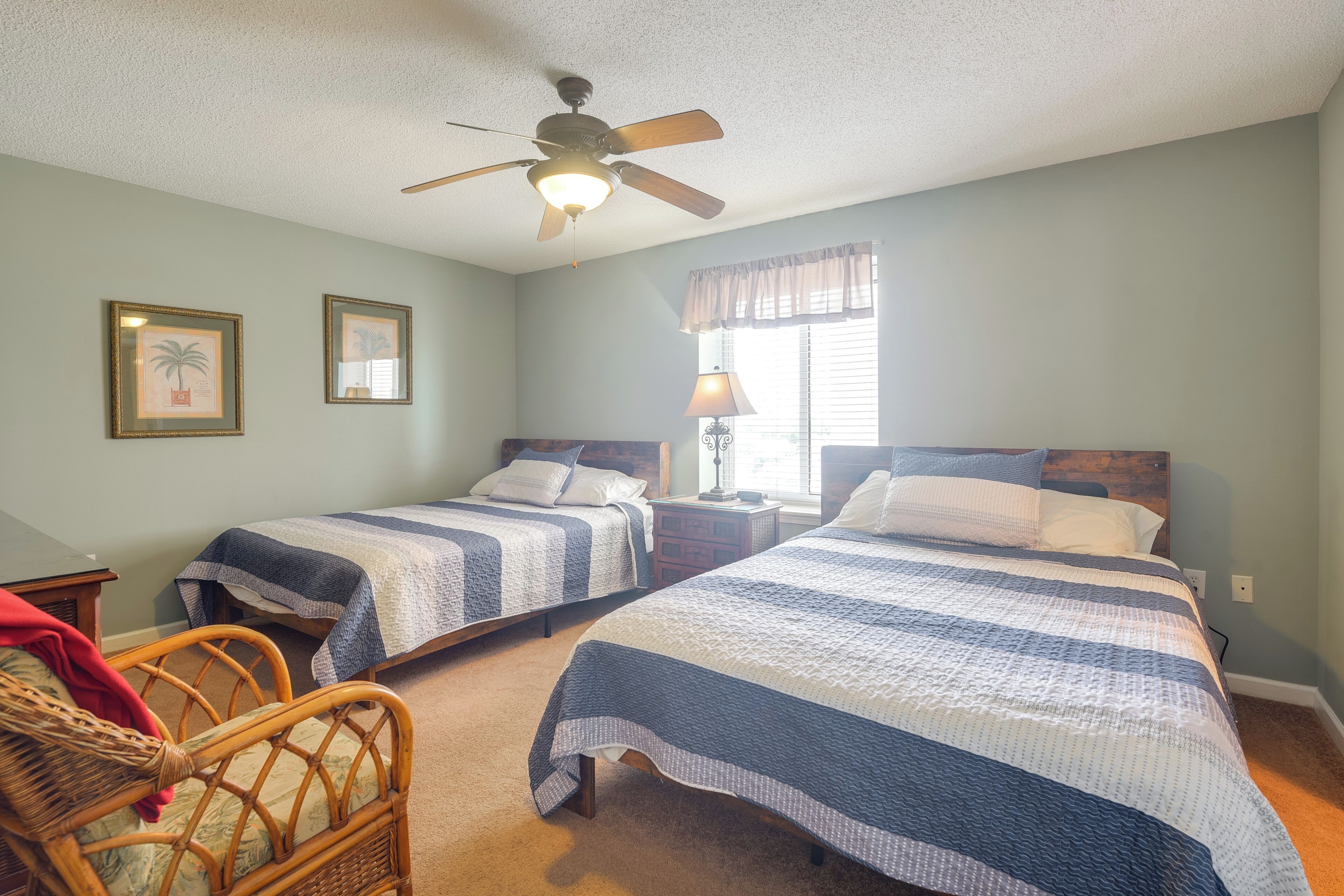 A bedroom with two beds, a ceiling fan, framed pictures on the wall, and a window with curtains.