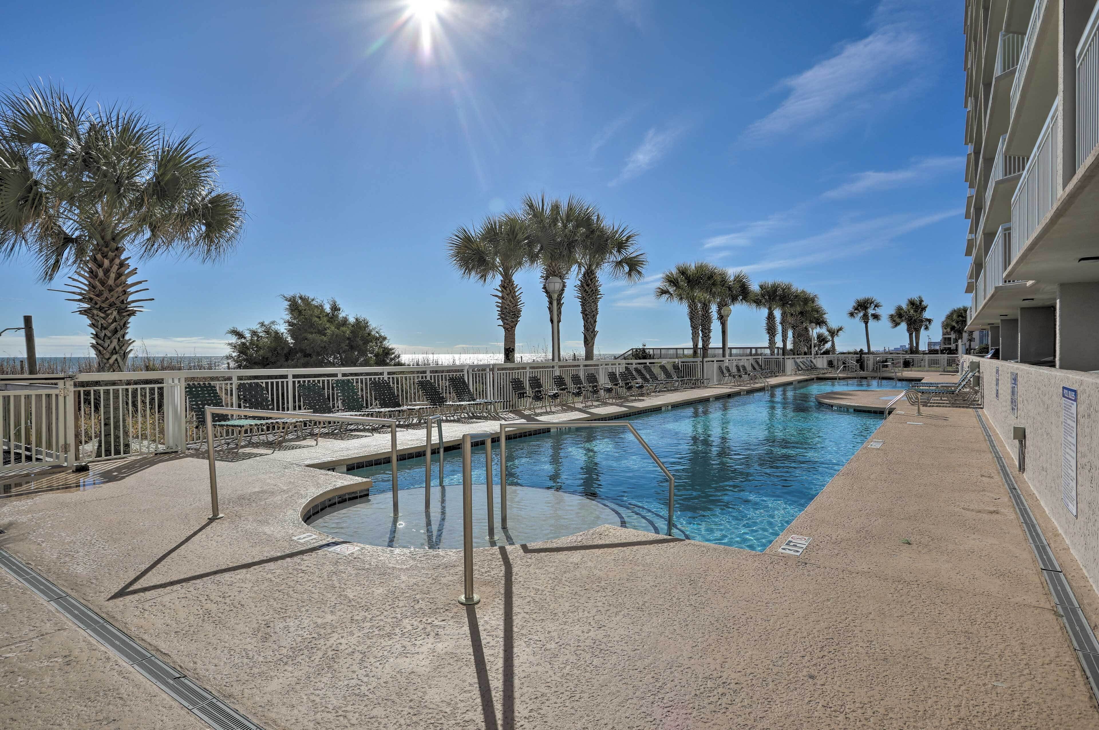 A pool area with palm trees, a clear sky, and a building with balconies.