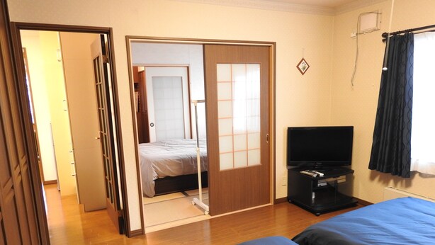A hotel room with a bed, a television, and a sliding door leading to another room. - Asahikawa Big Lodge 7 People (Asahikawa)
