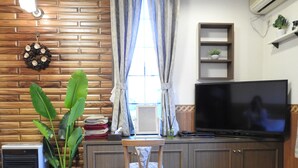 A compact living space with a wooden wall, a television, a small shelf with a plant, and a potted plant. - Asahikawa Big Lodge 7 People (Asahikawa)