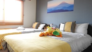 A hotel room with two beds, a large window with blinds, a painting of a mountain, and a plush toy on the bed. - Asahikawa Big House 10 People (Asahikawa)