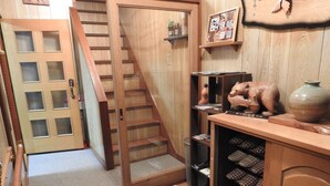 A wooden interior with a staircase, a shoe rack, and a shelf with decorative items. - Asahikawa Big House 10 People (Asahikawa)