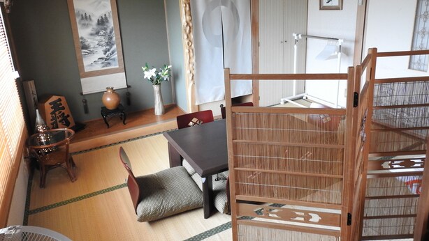 A traditional Japanese room with tatami flooring, a low table, a cushioned bench, and a sliding door. - Asahikawa Big House 10 People (Asahikawa)