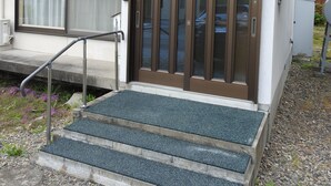 A building with a brown door, a small set of steps leading up to it, and a red railing on the upper level. - Asahikawa Big House 10 People (Asahikawa)