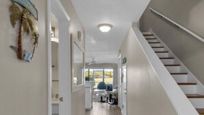 Un pasillo con una escalera, una puerta que da a una habitación y vistas al exterior.