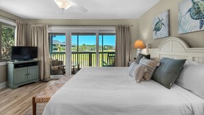 Un dormitorio con cama, televisor, ventilador de techo y vistas a un balcón con piscina.
