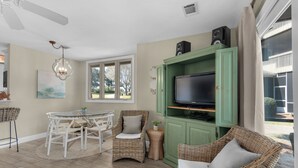 Una sala de estar con televisión, muebles de mimbre, una mesa de comedor y un ventilador de techo.
