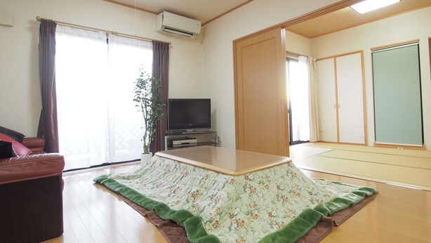 A spacious living room with a flat-screen TV, a sofa, a large window with curtains, and a sliding door leading to another room. - Okazaki House up to 8 People (Okazaki)