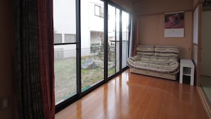 Una habitación con un amplio ventanal corredera que da a un balcón, un sofá a rayas, una pequeña mesa blanca y una lámpara colgante.