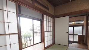 Una habitación japonesa tradicional con suelo de tatami, puertas correderas y vista a un barrio residencial.