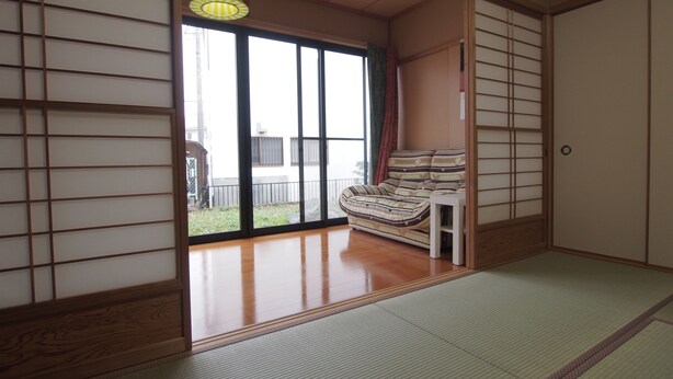 Una habitación japonesa tradicional con suelo de tatami, una mesa de madera baja, un sofá y un fusuma que da a un balcón.