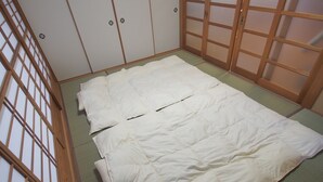 Una habitación con suelo de tatami, cama con ropa de cama blanca y puertas correderas tradicionales.