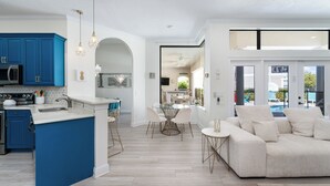 A modern kitchen with blue cabinets, a white island, and a dining area with a white table and chairs. - Rare Extended Pool Deck & Oversized Spa | Arcade Room | Kids Bedrooms (Kissimmee)