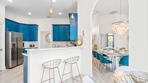 A modern kitchen with blue cabinets, a white island, bar stools, and a chandelier. - Rare Extended Pool Deck & Oversized Spa | Arcade Room | Kids Bedrooms (Kissimmee)