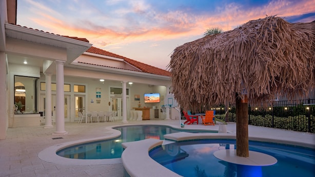 A swimming pool with a thatched structure, a covered seating area, and a view of the building's interior. - Rare Extended Pool Deck & Oversized Spa | Arcade Room | Kids Bedrooms (Kissimmee)