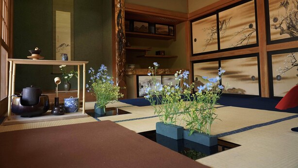 A traditional Japanese room with tatami flooring, a low table with a tea set, and a large window with a view of trees. - Kougetsu Sanso (Hachioji)