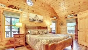 A wooden cabin bedroom with a large bed, wooden dresser, and a window with a view of trees. - 2-Tier Deck & Hot Tub: Quiet Sevierville Cabin (Sevierville)