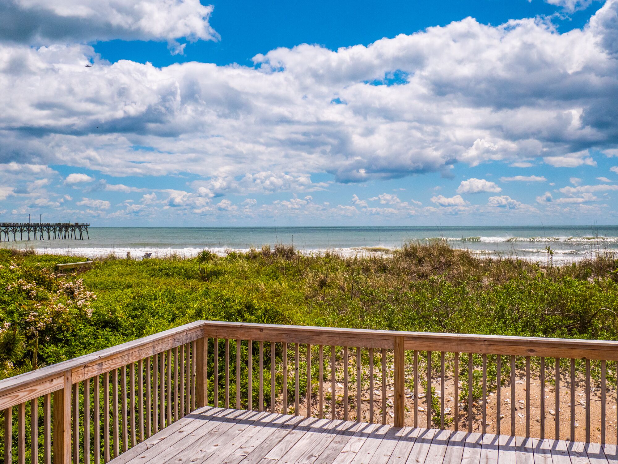 A wooden deck with a view of the beach and ocean.