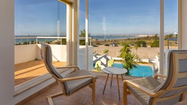 A balcony with two wicker chairs and a small table, overlooking a swimming pool and a parking area. - Villa Blue Ocean by Interhome (Gale)