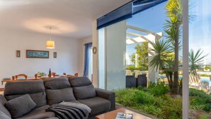 A modern living room with a grey sofa, a wooden coffee table, and a large glass window overlooking a pool and greenery. - Villa Blue Ocean by Interhome (Gale)