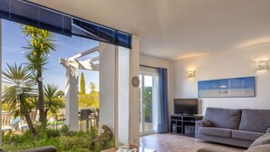 A modern living room with a grey sofa, a TV, and a dining area with a table and chairs. - Villa Blue Ocean by Interhome (Gale)