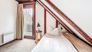 Ein Schlafzimmer mit schrägem Dach, einem Bett, einem Nachttisch, einer Lampe und Blick ins Freie.