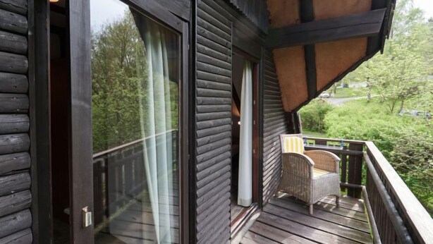 Eine Holzblockhütte mit einem Balkon, großen Schiebegläsern und Blick auf Grünflächen.