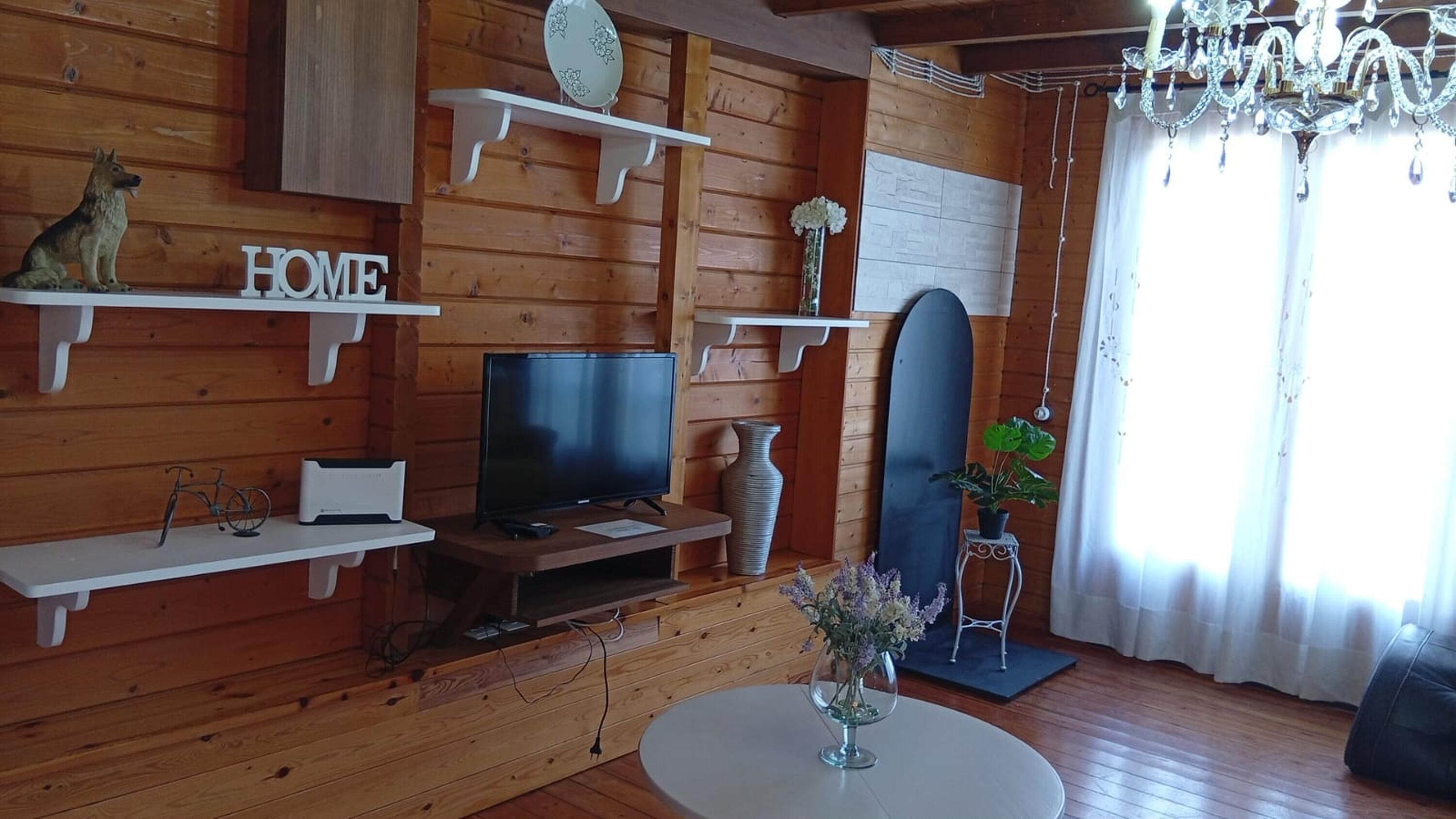 A wooden interior with a TV, shelves, a mirror, and a chandelier.