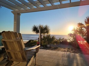 A wooden chair and a small table under a pergola overlooking a beach at sunset. - Want Beachfront? Book While You Can. Oceanfront-Family Friendly-Beach House (Ormond Beach)