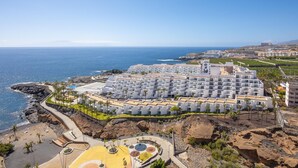 Un hotel costero con varias edificaciones blancas, una playa y terreno rocoso.