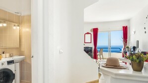 Un baño moderno con lavadora, un espejo grande y vista al mar desde un balcón.