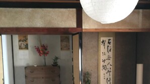 Ein traditioneller japanischer Raum mit Tatami-Böden, einer hölzernen Kommode, einer hängenden Papierlaterne und einem Shoji-Bildschirm mit Kalligraphie.
