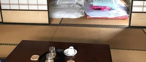 A traditional Japanese room with tatami flooring, a low wooden table with tea set, and futon beds.