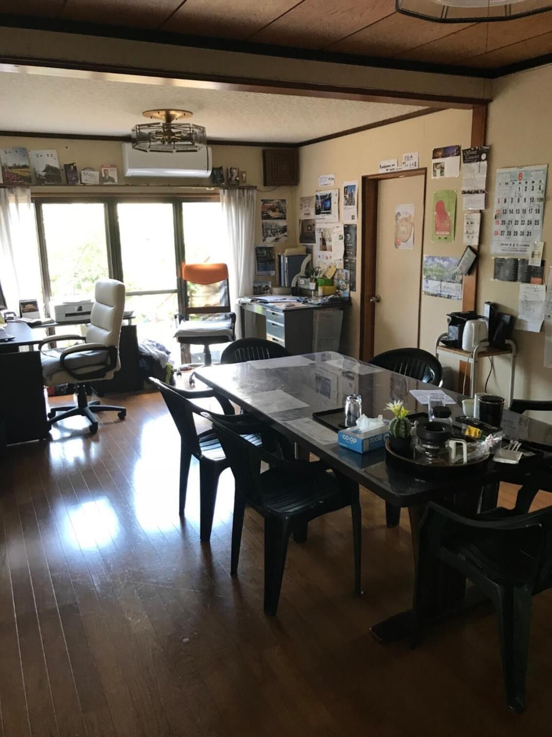 Uma sala de jantar com uma mesa comprida, várias cadeiras, um ventilador de teto e uma janela com cortinas.